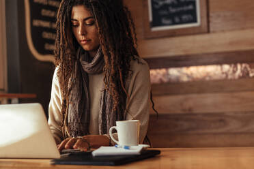 Frau sitzt in einem Restaurant und arbeitet an einem Laptop. Freiberufler sitzt in einem Café mit einem Kaffee und einem Notizblock und arbeitet an einem Laptop-Computer. - JLPSF26644