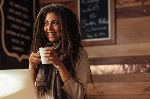 Lächelnde Frau, die in einem Café steht und eine Tasse Kaffee in der Hand hält. - JLPSF26646