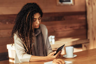 Frau sitzt in einem Restaurant und benutzt ihr Mobiltelefon. Frau sitzt in einem Café mit Kaffee und Snacks auf dem Tisch. - JLPSF26649