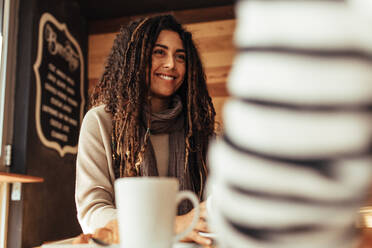 Lächelnde Frau, die in einem Restaurant sitzt und sich mit ihrer Freundin unterhält. Freunde sitzen in einem Café mit Kaffee auf dem Tisch. - JLPSF26651