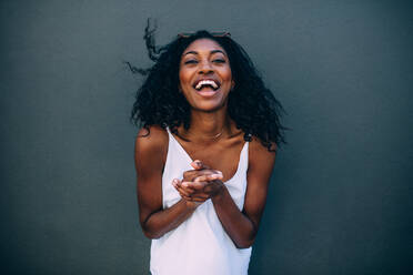 Woman in joyful mood clapping her hands. Portrait of a curly haired woman jumping with joy clapping hands standing against a wall. - JLPSF26682