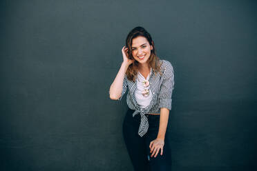 Portrait of a smiling woman wearing fashionable clothes standing against a wall. Happy looking woman standing against a wall. - JLPSF26688