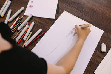 Unternehmerin, die an ihrem Tisch einen Entwurf skizziert. Ausschnitt einer Modedesignerin, die an ihrem Schreibtisch eine Zeichnung anfertigt. - JLPSF26695