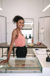 Weibliche Modedesignerin steht an ihrem Schreibtisch in ihrer Boutique. Lächelnde weibliche Kleiderdesignerin in ihrem Stoffladen. - JLPSF26710