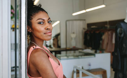 Female fashion designer standing in her boutique. Female dress designer in her cloth shop with designer clothes on display. - JLPSF26712