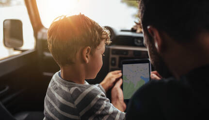 Rückansicht von Vater und Sohn, die im Auto sitzen und die Route einer Autoreise mit einem digitalen Tablet planen. Mann mit kleinem Jungen, der eine Navigations-App auf einem digitalen Tablet benutzt. - JLPSF26715