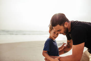 Outdoor shot of young man with his son at the beach. Father and son on sea shore during summer vacation. - JLPSF26732