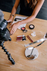 Eine Frau macht ein Video für ihren Blog über Kosmetika. Eine junge Frau mit Kosmetikartikeln auf einem Tisch nimmt ihr Video mit einer auf einem Stativ montierten Kamera auf. - JLPSF26761