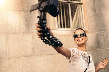 Weibliche Vloggerin, die Inhalte für ihren Vlog aufnimmt. Junge Frau, die mit einer Digitalkamera auf einem flexiblen Stativ ein Selfie auf einer Straße macht. - JLPSF26764