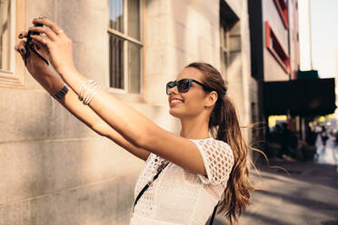 Vlogger recording content for her travel vlog. Young woman taking selfie in a street using a digital camera. - JLPSF26765