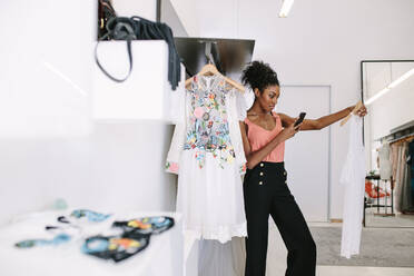 Fashion designer taking photograph of a designer dresses in her fashion studio. Customer taking photograph of dress in a fashion clothes shop. - JLPSF26784