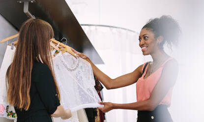 Eine Kundin sieht sich in einer Boutique Kleider an. Eine Unternehmerin zeigt einer Kundin Designerkleidung. - JLPSF26789