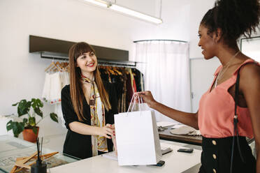 Eine Kundin kauft in einer Modeboutique Designerkleidung ein. Eine Unternehmerin überreicht der Kundin eine Einkaufstasche. - JLPSF26794