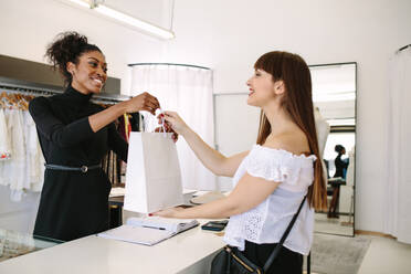 Eine Kundin kauft in einer Modeboutique Designerkleidung ein. Eine Unternehmerin überreicht der Kundin eine Einkaufstasche. - JLPSF26801