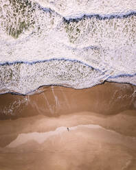 Luftaufnahme einer Person am Strand entlang der Küstenlinie in Caparica Beach, Lissabon, Portugal. - AAEF16545