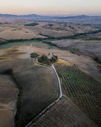 Siena, Toskana - 05. September 2021: Luftaufnahme eines kleinen Hauses auf einer Hügelkuppe, umgeben von Weinbergen, bei Sonnenuntergang im Val d'Orcia, Toskana, Italien. - AAEF16555