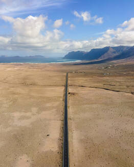 Luftaufnahme einer geraden Straße durch ein Wüstental bei Caleta de Famara auf Lanzarote, Kanarische Inseln, Spanien. - AAEF16581