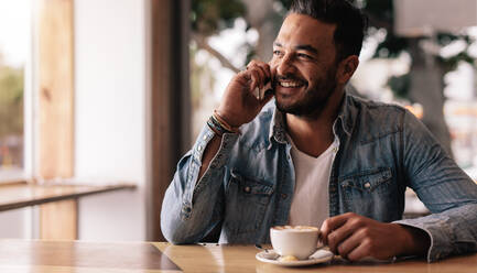 Innenaufnahme eines jungen Mannes, der in einem Café sitzt und mit einem Mobiltelefon spricht. Ein gut aussehender weißer Mann im Café telefoniert und schaut weg. - JLPSF26803