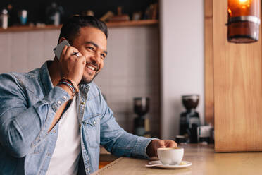 Indoor shot of handsome young man in coffee shop talking on mobile phone. Caucasian guy sitting at cafe making a phone call and looking away. - JLPSF26804