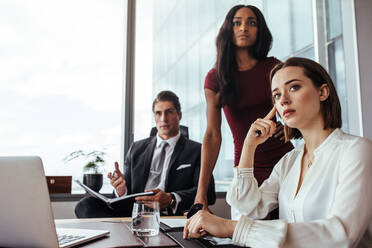 Drei Geschäftsleute, die am Schreibtisch sitzen und sich um etwas Wichtiges kümmern. Junge Frau mit Kollegen während einer Besprechung im Büro. - JLPSF26808