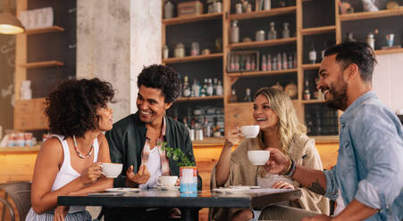 Junge Leute sitzen in einem Café und unterhalten sich. Eine Gruppe von Freunden trinkt gemeinsam Kaffee in einem Café. - JLPSF26816