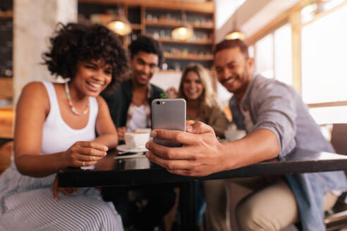 Junge Männer und Frauen sitzen zusammen im Café und nehmen ein Selbstporträt auf dem Handy. Kleine Gruppe von Freunden, die Selfie auf dem Handy. - JLPSF26820