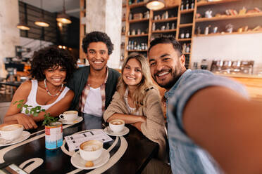 Happy young man taking selfie with friends in a cafe. Young multiracial people in a coffee shop making a self portrait. - JLPSF26821