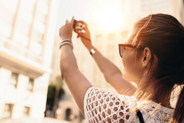 Vlogger recording content for her travel vlog. Young woman taking selfie in a street using a digital camera. - JLPSF26836