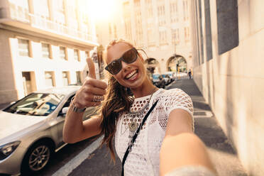 Tourist posiert für ein Selfie in einer Straße mit Daumen hoch-Zeichen. Vloggerin nimmt Inhalte für ihren Reise-Vlog auf. - JLPSF26838