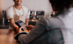 Ausschnitt eines Kunden, der seine PIN-Nummer in ein Gerät am Schalter eines Cafés eingibt; Fokus auf die Hände einer Frau, die die Sicherheitsnummer in das Kreditkartenlesegerät eingibt. - JLPSF26853