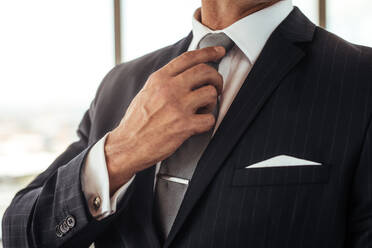 Cropped shot of businessman hand adjusting his necktie. Close up of man in business suit correcting tie. - JLPSF26865
