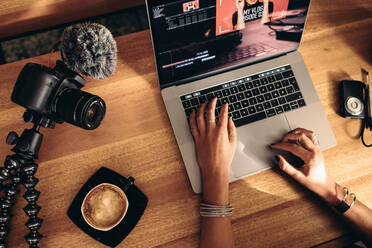 Blick von oben auf eine Vloggerin, die ein Video am Laptop bearbeitet. Junge Frau arbeitet am Computer mit Kaffee und Kameras auf dem Tisch. - JLPSF26867