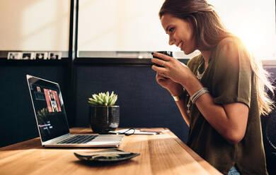 Junge Frau, die ein Video auf ihrem Laptop bearbeitet, während sie Kaffee trinkt. Vloggerin, die ihren Vlog mit einer Tasse Kaffee genießt. - JLPSF26868