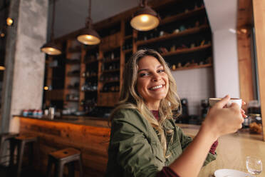 Porträt einer schönen jungen Frau, die mit einer Tasse Kaffee im Café sitzt und lächelt. Kaukasische Frau trinkt Kaffee im Café. - JLPSF26874