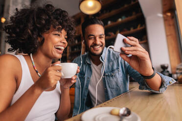 Junger Mann zeigt seiner Freundin im Café etwas auf dem Handy. Glückliches junges Paar sitzt im Café und führt einen Videochat auf dem Handy. - JLPSF26894