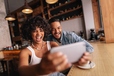 Glückliches junges Paar, das zusammen in einem Café sitzt und ein Selfie mit dem Handy macht. Afrikanische Frau mit ihrem Freund, die ein Selbstporträt mit einem Smartphone machen. - JLPSF26897