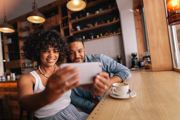 Schönes junges Paar, das zusammen in einem Café sitzt und ein Selfie mit dem Handy macht. Afrikanische Frau mit ihrem Freund, die ein Selbstporträt mit einem Smartphone machen. - JLPSF26900
