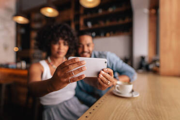 Nahaufnahme von weiblichen Händen, die ein Mobiltelefon halten und ein Selbstporträt machen. Junge Frau, die ein Selfie mit ihrem Smartphone macht, während sie mit ihrem Freund im Café sitzt. - JLPSF26901