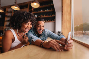 Junges Paar sitzt zusammen in einem Café und macht ein Selfie mit dem Smartphone. Junger Mann und Frau lachen, während sie ein Selfie im Café machen - JLPSF26905