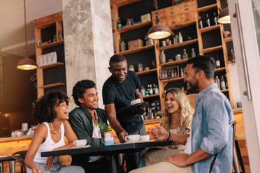 Group of friends sitting around table and waiter serving coffee at cafe. Young people meeting at coffee shop. - JLPSF26908