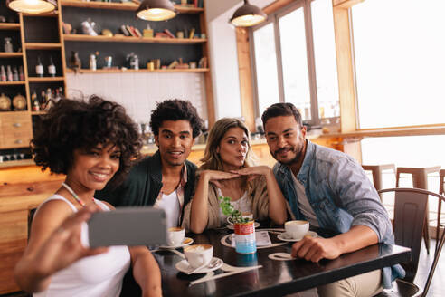 Junge Männer und Frauen sitzen zusammen im Café und nehmen ein Selbstporträt auf dem Handy. Kleine Gruppe von Freunden, die Selfie auf dem Handy. - JLPSF26915