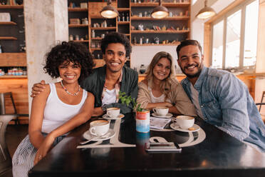 Porträt einer Gruppe von Freunden, die in einem Café zusammensitzen. Junge Leute treffen sich in einem Café, schauen in die Kamera und lächeln. - JLPSF26918