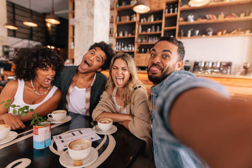 Junger Mann macht Selfie mit Freunden, die in einem Café lustige Gesichter machen. Verrückte junge Leute in einem Café machen ein Selbstporträt. - JLPSF26919