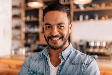 Close up portrait of handsome young man standing in a cafe. Smiling young caucasian male in a coffee shop. - JLPSF26920