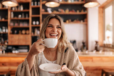 Porträt einer schönen jungen Frau, die in einem Café steht und Kaffee trinkt. Lächelnde junge Frau beim Kaffeetrinken in einem Restaurant. - JLPSF26924