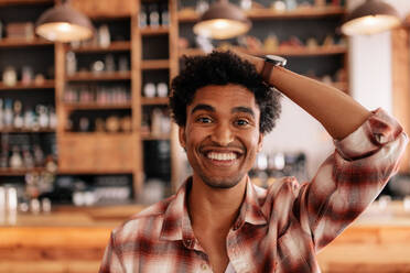 Close up Porträt von glücklichen jungen Mann lächelnd in einem Café mit der Hand auf dem Kopf. Junge afrikanische männliche in einem Café Spaß haben. - JLPSF26929