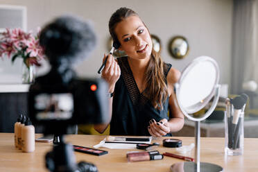 Young lady recording her video while applying cosmetics. Woman making a video for her blog on cosmetics. - JLPSF26945