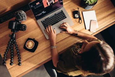 Blick von oben auf eine Vloggerin, die ein Video am Laptop bearbeitet. Junge Frau arbeitet am Computer mit Kaffee und Kameras auf dem Tisch. - JLPSF26959