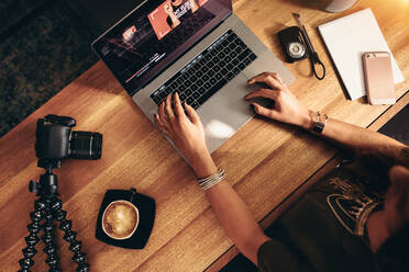 Blick von oben auf eine Vloggerin, die ein Video am Laptop bearbeitet. Junge Frau arbeitet am Computer mit Kaffee und Kameras auf dem Tisch. - JLPSF26961