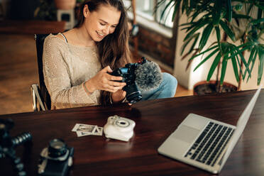 Eine Bloggerin, die ihre aufgezeichneten Inhalte vor der Kamera betrachtet, mit Laptop und Kameras auf dem Tisch. Eine Bloggerin, die zu Hause sitzend die aufgezeichneten Inhalte für ihren Blog überprüft. - JLPSF26998